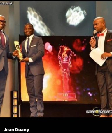 Deux hommes en costume reçoivent un prix sur scène, avec un présentateur en arrière-plan.