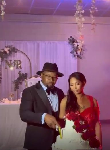 Un couple élégant coupe un gâteau de mariage devant une décoration romantique.